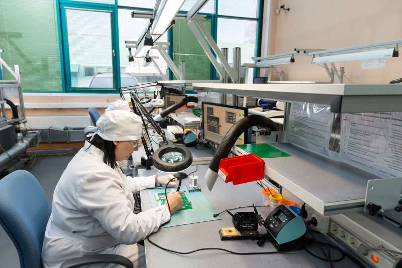 Person im Elektroniklabor bearbeitet Leiterplatten; Fokus auf embedded hardware und Qualitätsprüfung.