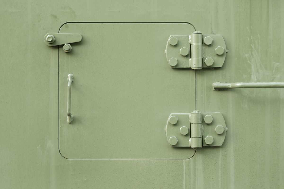 Grüne Metalltür mit Griff, Bolzen und schweren Scharnieren – Beispiel für embedded hardware.